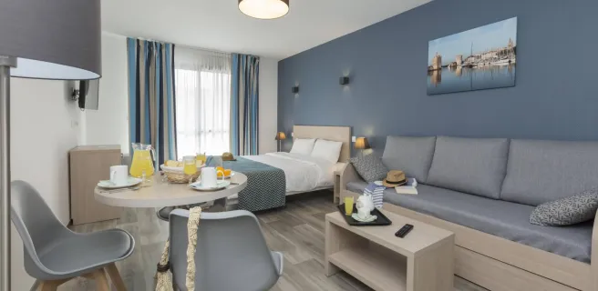 Appartement avec lit double, canapé, table basse, table avec petit-déjeuner et deux chaises.