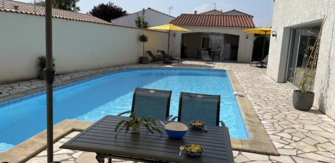 La terrasse avec piscine découverte, un salon de jardin métallique et un parasol sur pied.