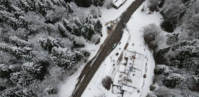 Vue drone du gîte et auberge de Carri à La Chapelle en Vercors, avec la route enneigée qui serpente à travers une forêt hivernale,.